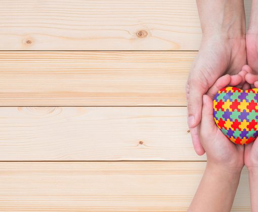 World Autism Awareness day, mental health care concept with puzzle or jigsaw pattern on heart with autistic child's hands supported by nursing family caregiver parent