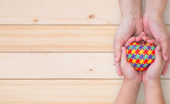 World Autism Awareness day, mental health care concept with puzzle or jigsaw pattern on heart with autistic child's hands supported by nursing family caregiver parent